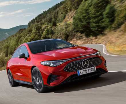 Vue de trois quarts avant d'une Mercedes-Benz CLA 2026 rouge roulant sur une route de campagne sinueuse à travers les montagnes.
