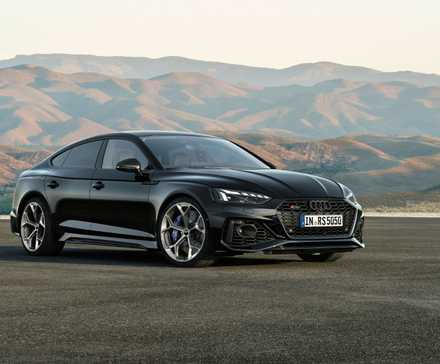 Vue complète d'une Audi RS5 Sportback noire garée sur le tarmac avec des montagnes en arrière-plan.
