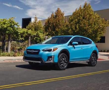 Vue complète d’une Subaru Crosstrek hybride 2020 bleue roulant sur une route traversant une ville.
