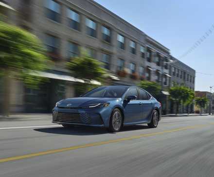 Vue 3/4 avant d'une Toyota Camry 2025 bleue traversant une ville.