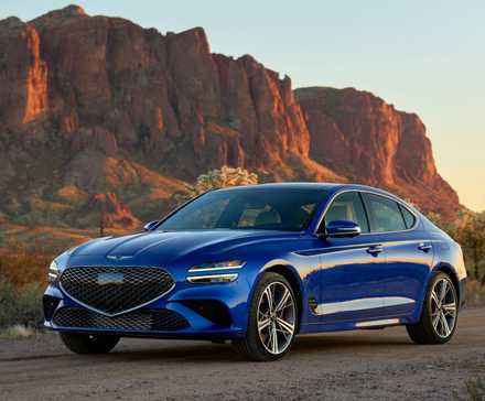 Plan 3/4 avant d'une Genesis G70 2025 bleue garée sur du gravier avec une montagne en arrière-plan.