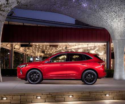 Photo de profil latérale statique d'un Ford Escape ST-Line Elite 2023 rouge garé à l'extérieur d'un bâtiment moderne.