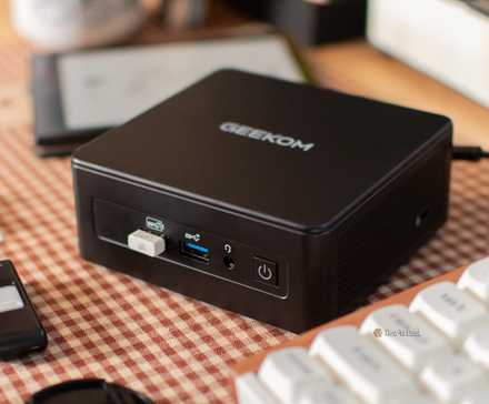 Le mini PC GEEKOM IT15 sur un bureau avec un clavier et une liseuse.