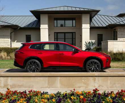 Photo de profil latérale statique d'une Toyota Crown Signia Limited 2025 rouge garée à l'extérieur d'une maison.