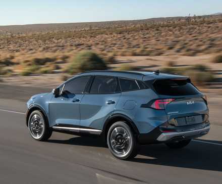 Plan 3/4 arrière dynamique d'un Kia Sportage HEV 2026 roulant sur une route de campagne.