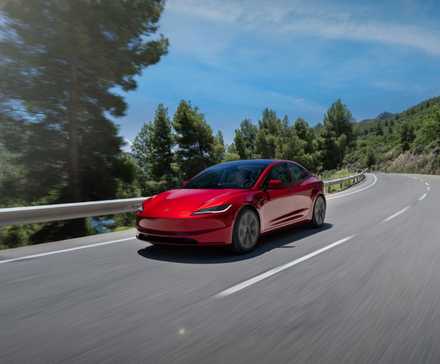 Plan 3/4 avant d'une Tesla Model 3 2024 rouge roulant sur une route de campagne sinueuse.