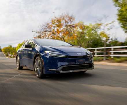 Vue 3/4 avant d'une Toyota Prius 2025 bleu marine roulant sur une route de campagne.